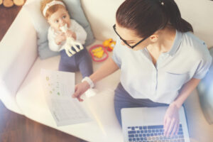 A parent working remotely from home with a child in the background, illustrating flexible work arrangements in Riverside custody cases.
